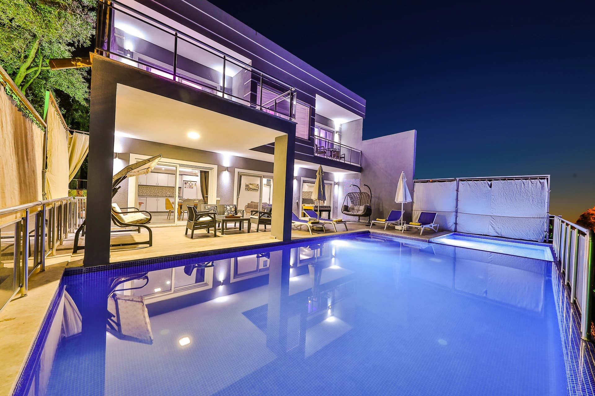 Resort-style pool with lounging area facing lit interior spaces and modern architecture.