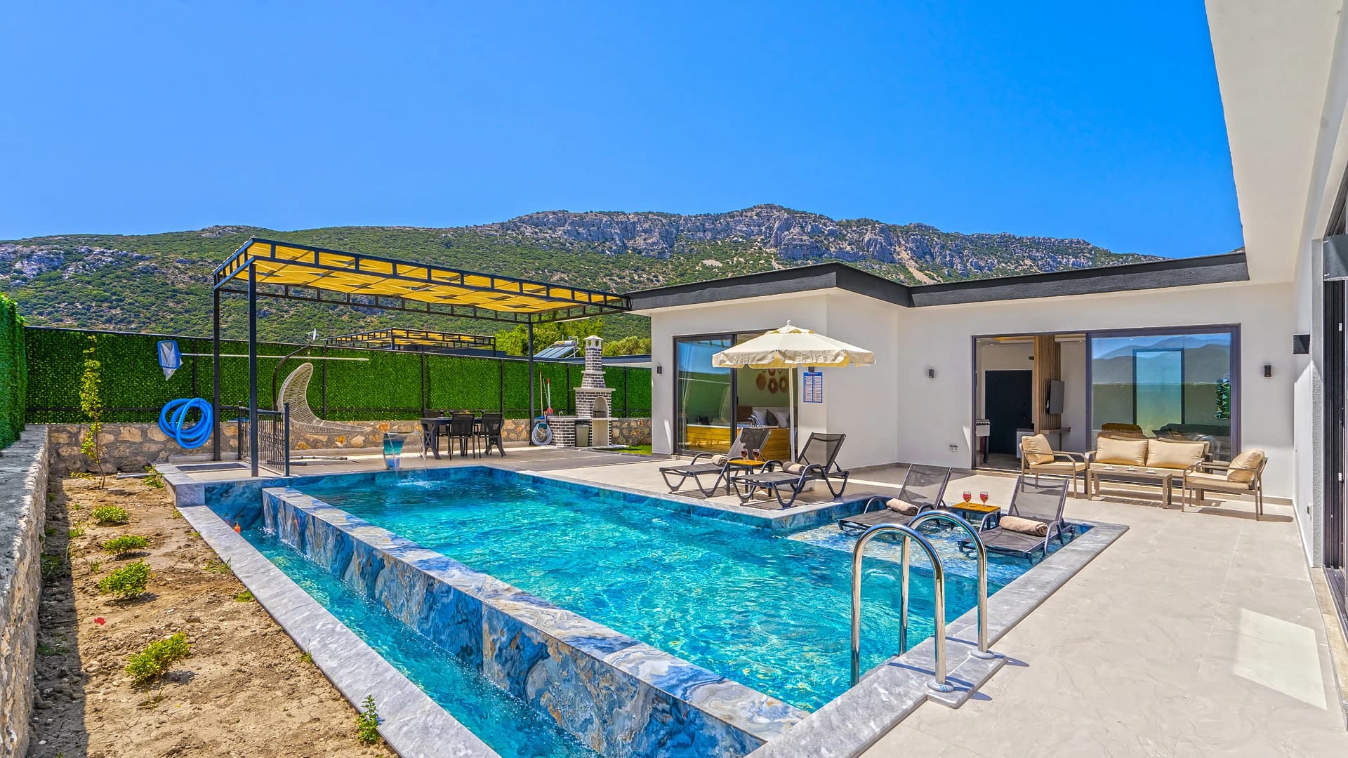 Stunning resort-style pool area with loungers, pergola shade, and mountain backdrop.
