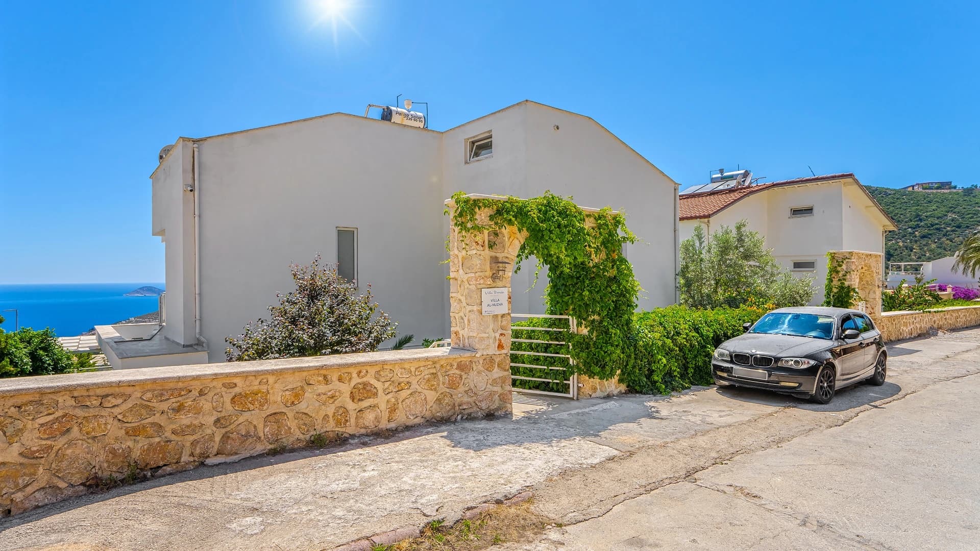 Front exterior of villa with stone architecture and parking area overlooking the sea.
