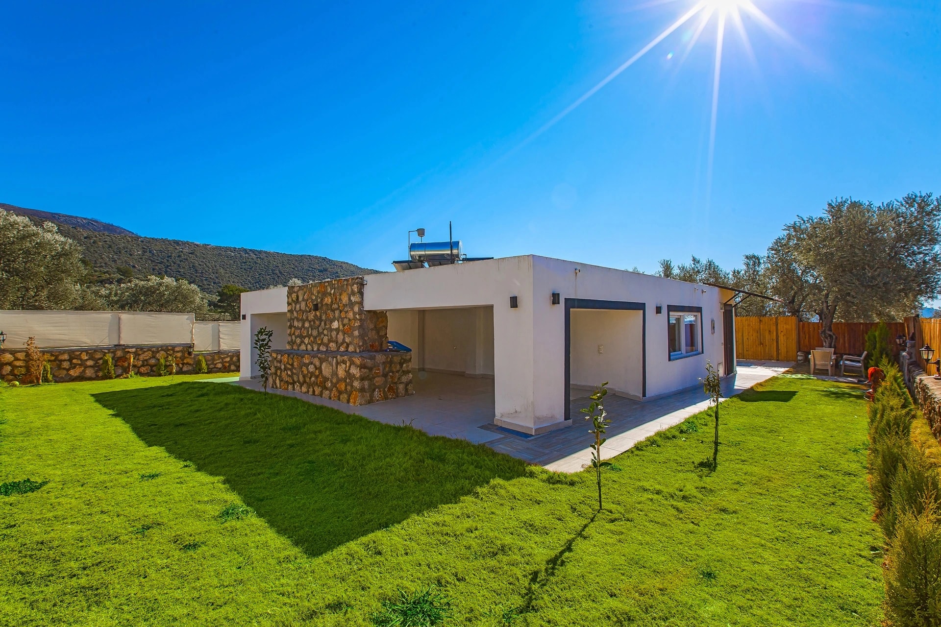 Kalkan Yakınlarında Orman İçinde Korunaklı, Özel Havuzlu ve Jakuzili Villa – Villa front elevation showcasing clean modern design with stone features and scenic mountain surroundings.
