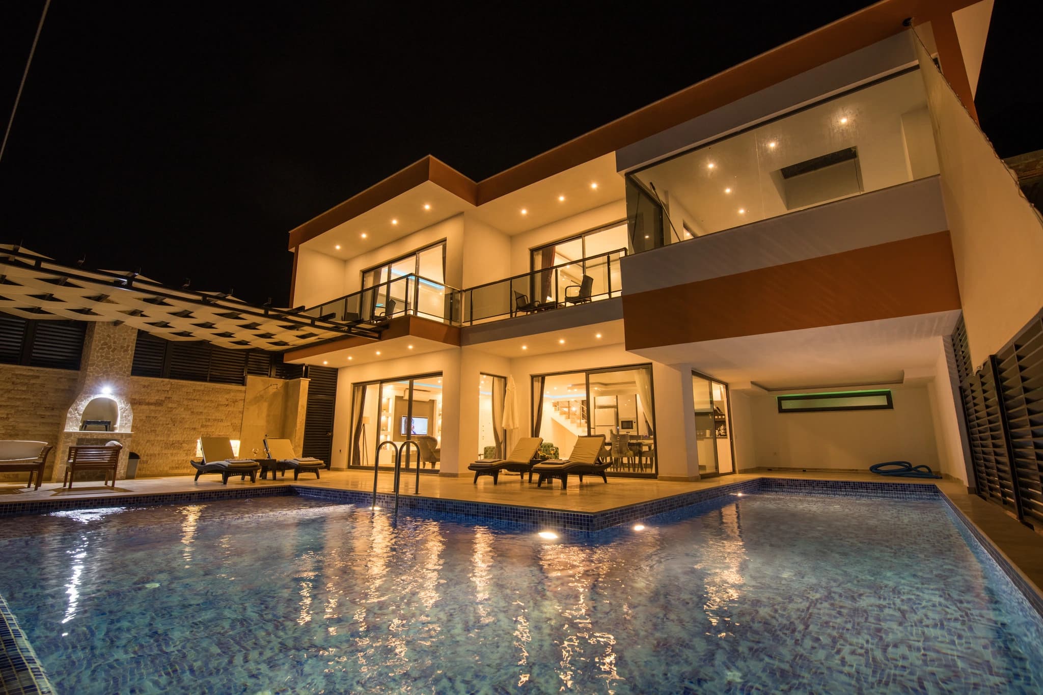 Kalkan'da Deniz Manzaralı, İç ve Dış Havuzlu Korunaklı Balayı Villası – Beautifully illuminated villa facade at night with glowing pool and terrace.