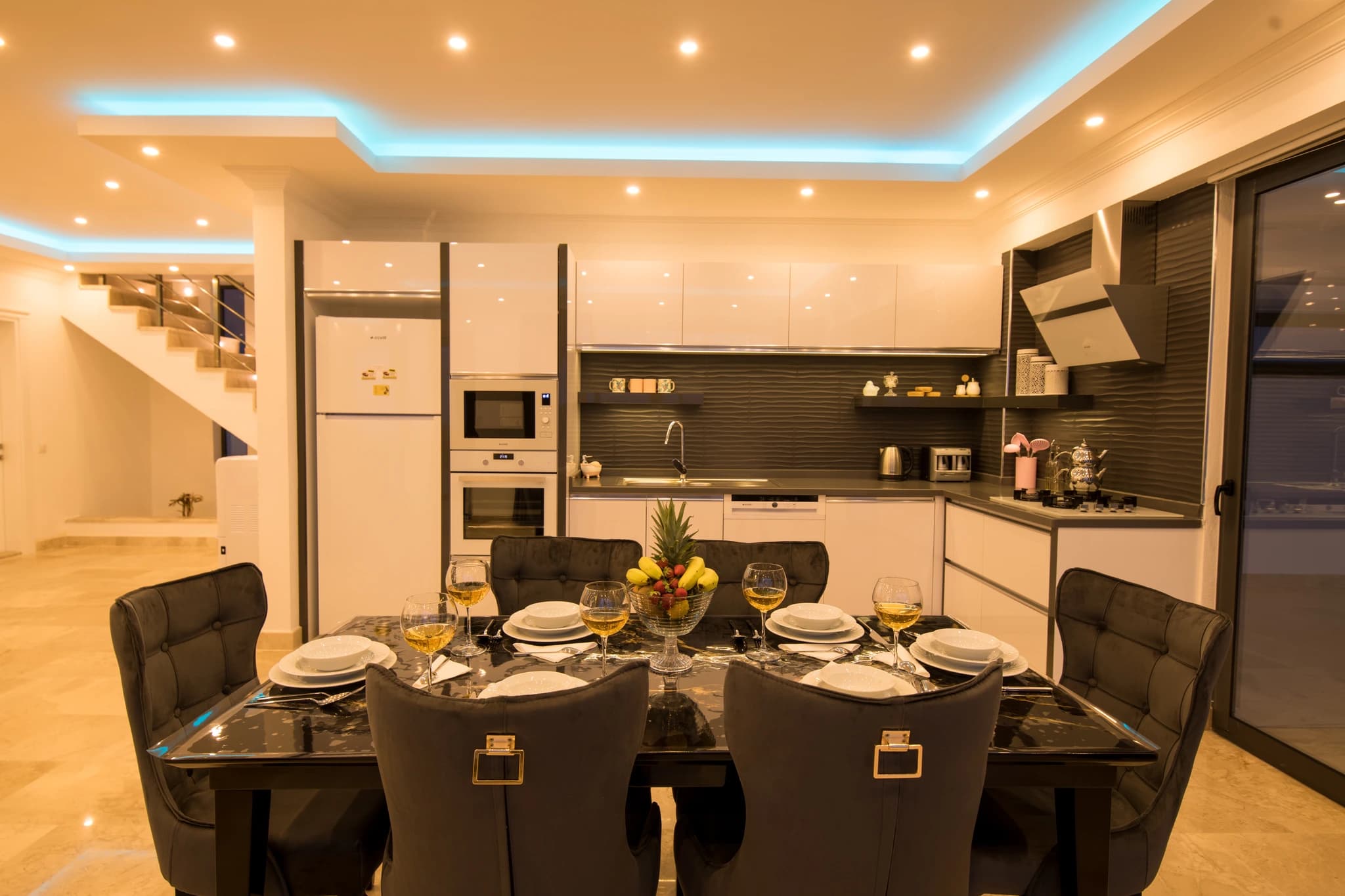Kalkan'da Deniz Manzaralı, İç ve Dış Havuzlu Korunaklı Balayı Villası – Open-plan kitchen and dining area with black marble table and modern appliances.