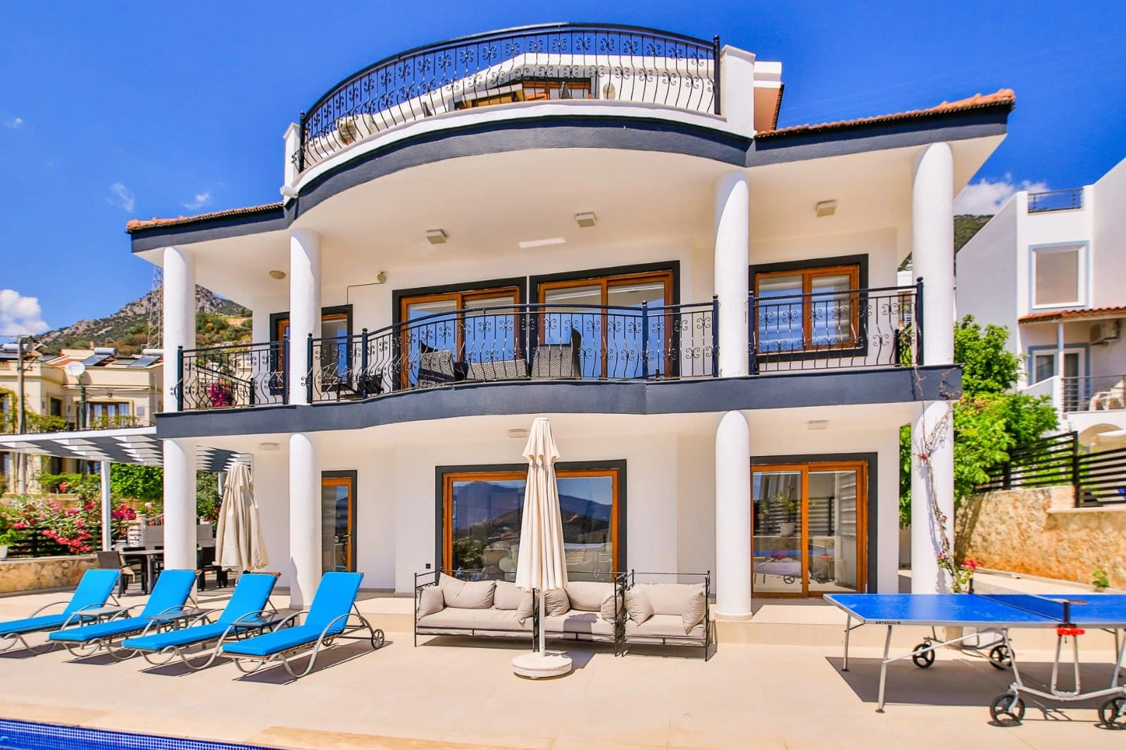 Contemporary villa exterior with curved balcony, private pool, and garden landscaping.