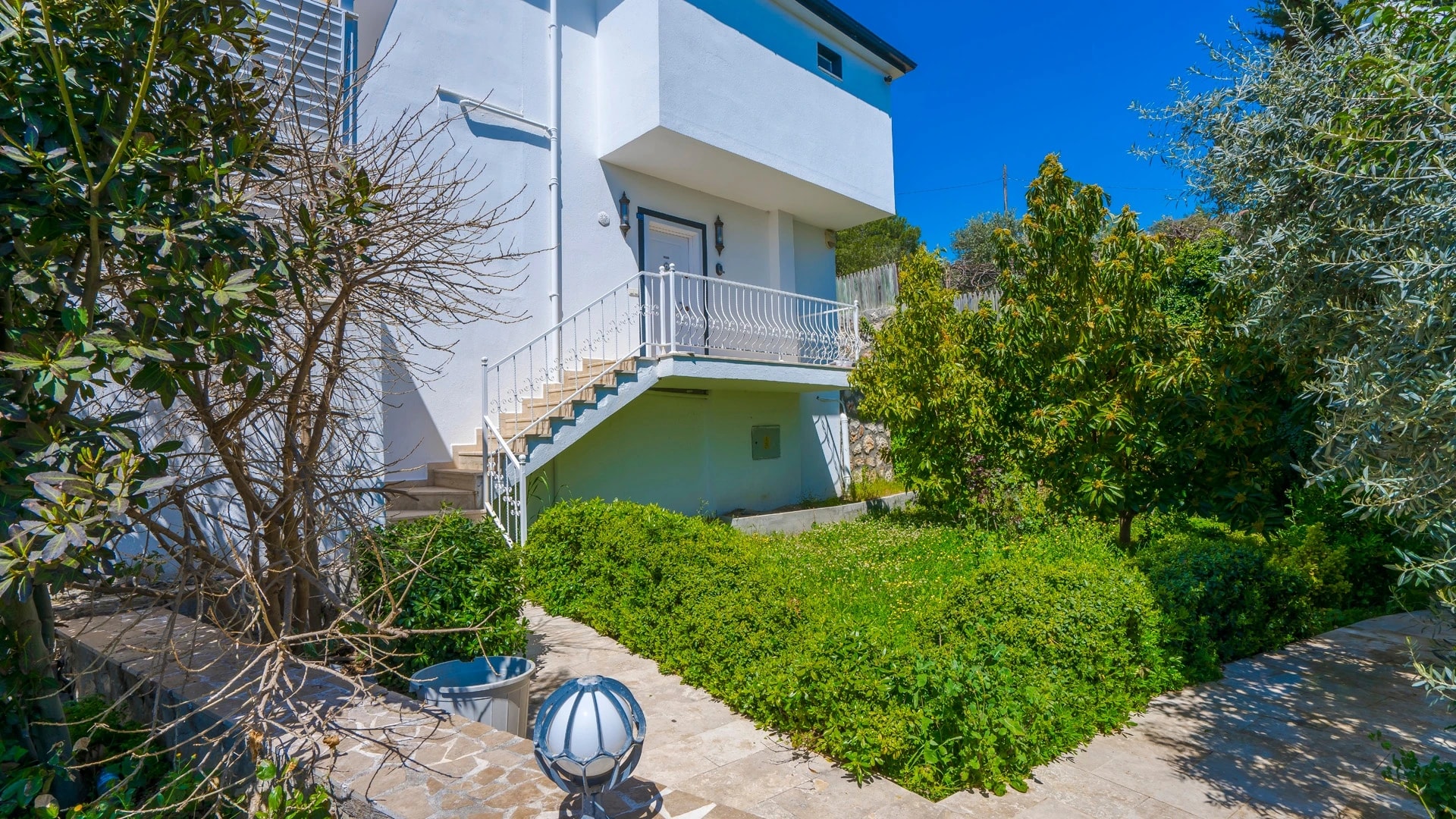 Kalkan'da Doğa İçinde Korunaklı, Isıtmalı Havuzlu, Deniz ve Dağ Manzaralı Villa – Modern villa exterior with white and blue contemporary design surrounded by lush greenery.