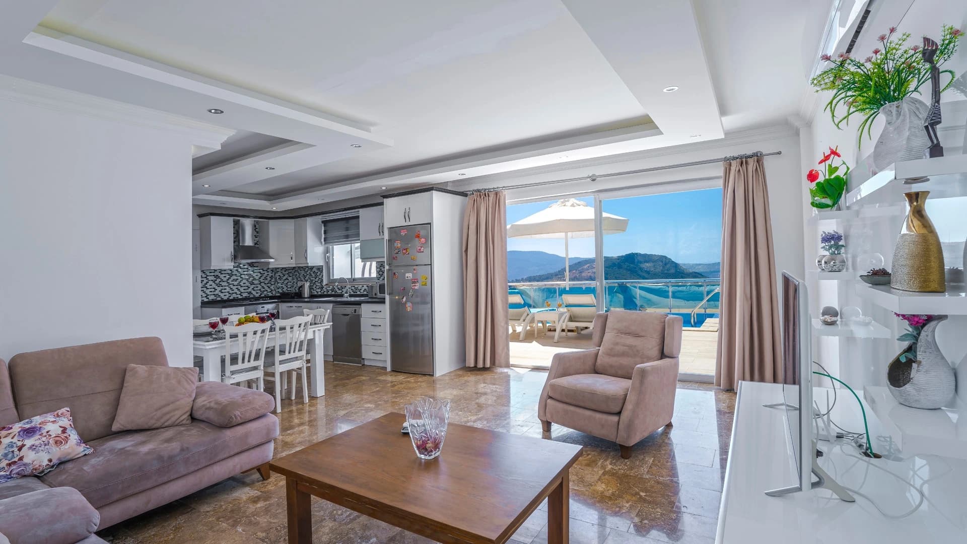 Kalkan'da Doğa İçinde Korunaklı, Isıtmalı Havuzlu, Deniz ve Dağ Manzaralı Villa – Spacious open-plan living room with sofas, sea and mountain views through large windows.