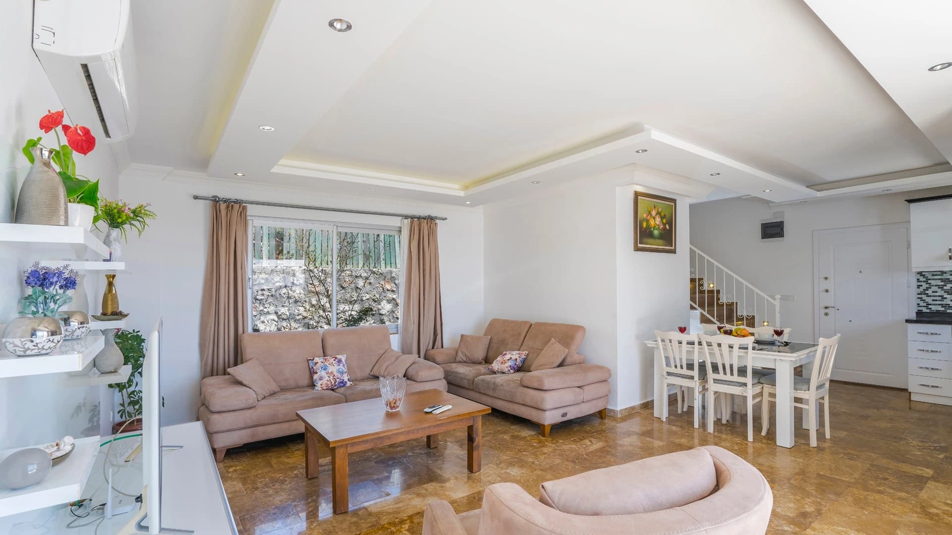Kalkan'da Doğa İçinde Korunaklı, Isıtmalı Havuzlu, Deniz ve Dağ Manzaralı Villa – Bright living room with two sofas, dining area, and staircase access to upper floor.