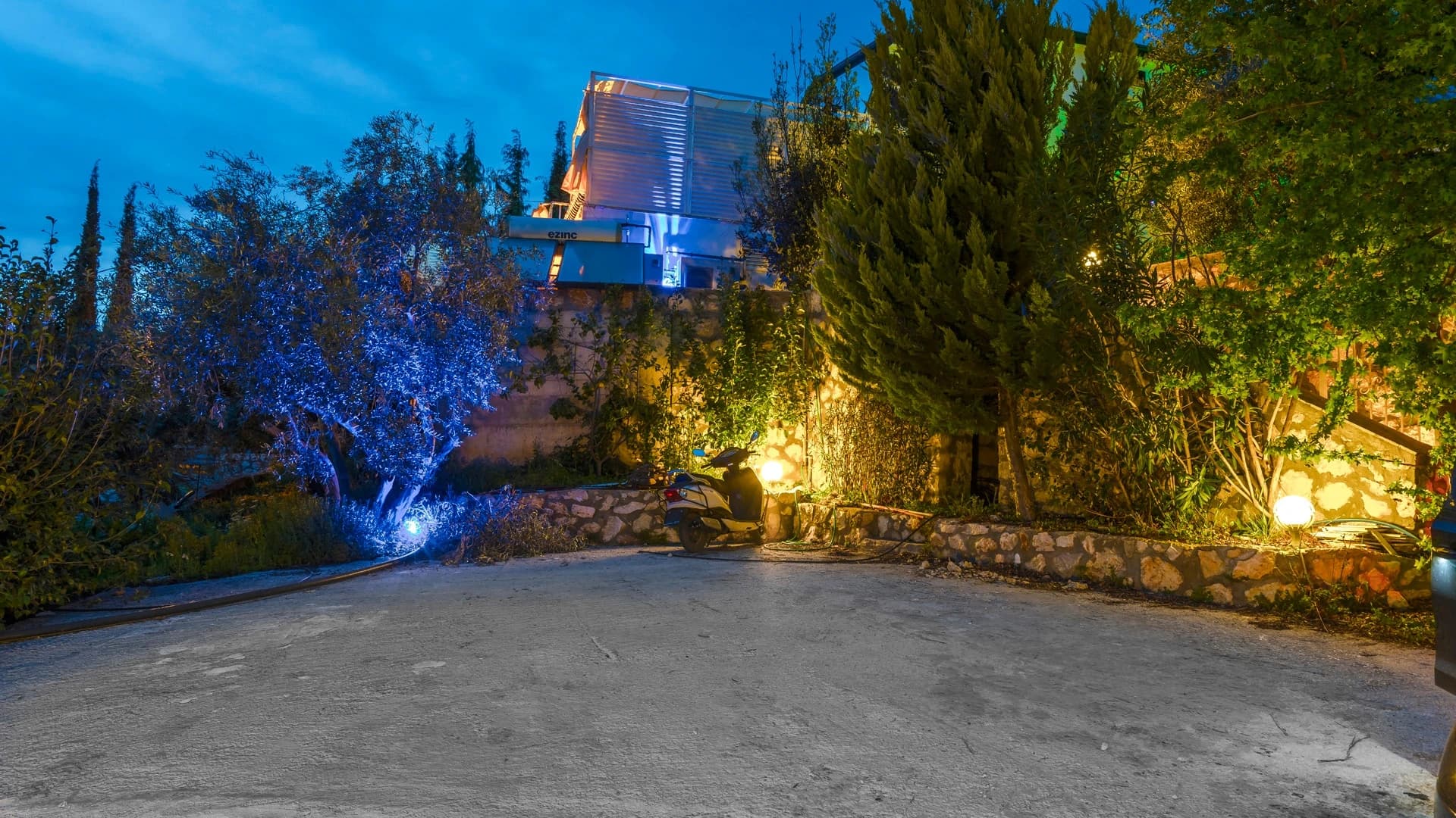 Kalkan'da Doğa İçinde Korunaklı, Isıtmalı Havuzlu, Deniz ve Dağ Manzaralı Villa – Elegant villa entrance with dramatic nighttime illumination, cypress landscaping, and stone architecture.