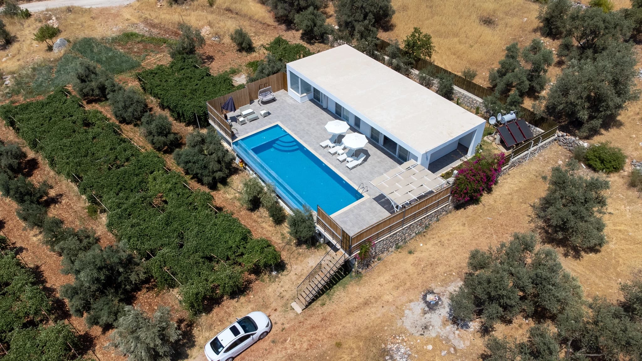 Kalkan Yakınında Sonsuzluk Havuzlu ve Dağ Manzaralı, Korunaklı 2 Yatak Odalı Villa – Aerial view of modern villa with rectangular pool, lounge areas, and surrounding Mediterranean landscape.