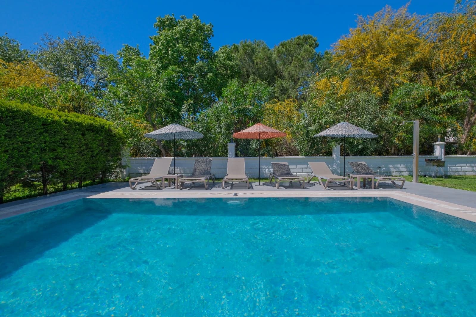 Crystal-clear swimming pool with multiple sun loungers and shaded umbrellas overlooking manicured gardens.