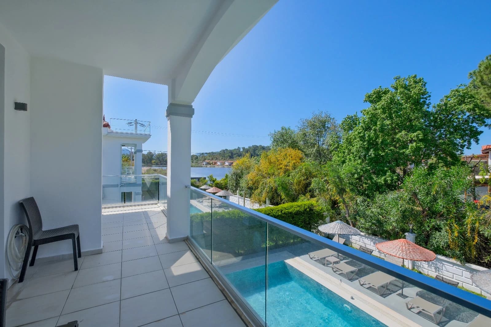 Modern balcony with glass railings offering scenic views of the pool, river, and surrounding landscape.