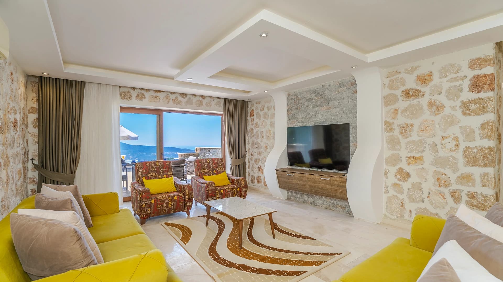 Contemporary living room with embedded smart TV, comfortable seating, and sea view access.