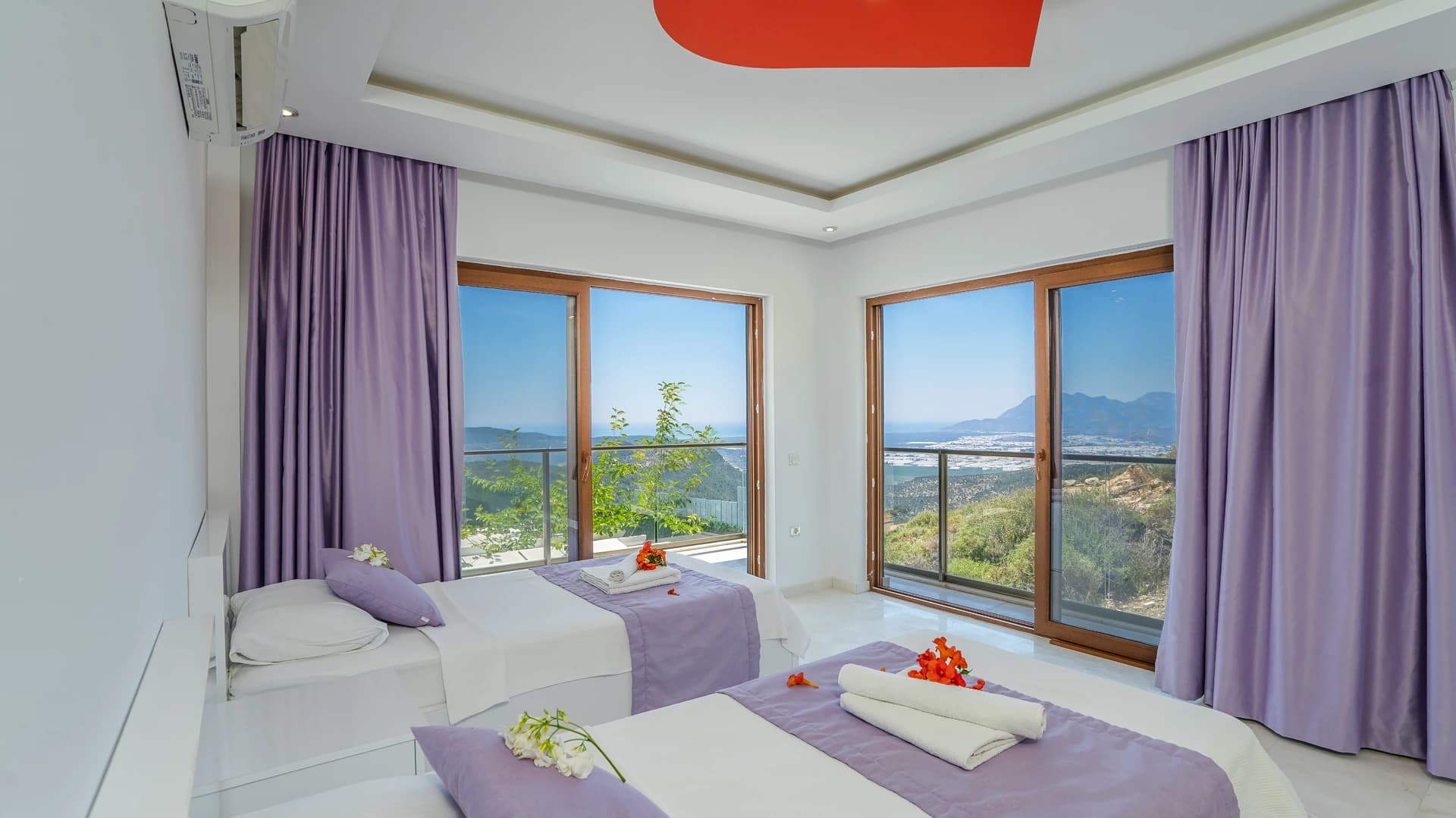 Bright bedroom with twin beds, purple accents, and expansive mountain and sea views from balcony.