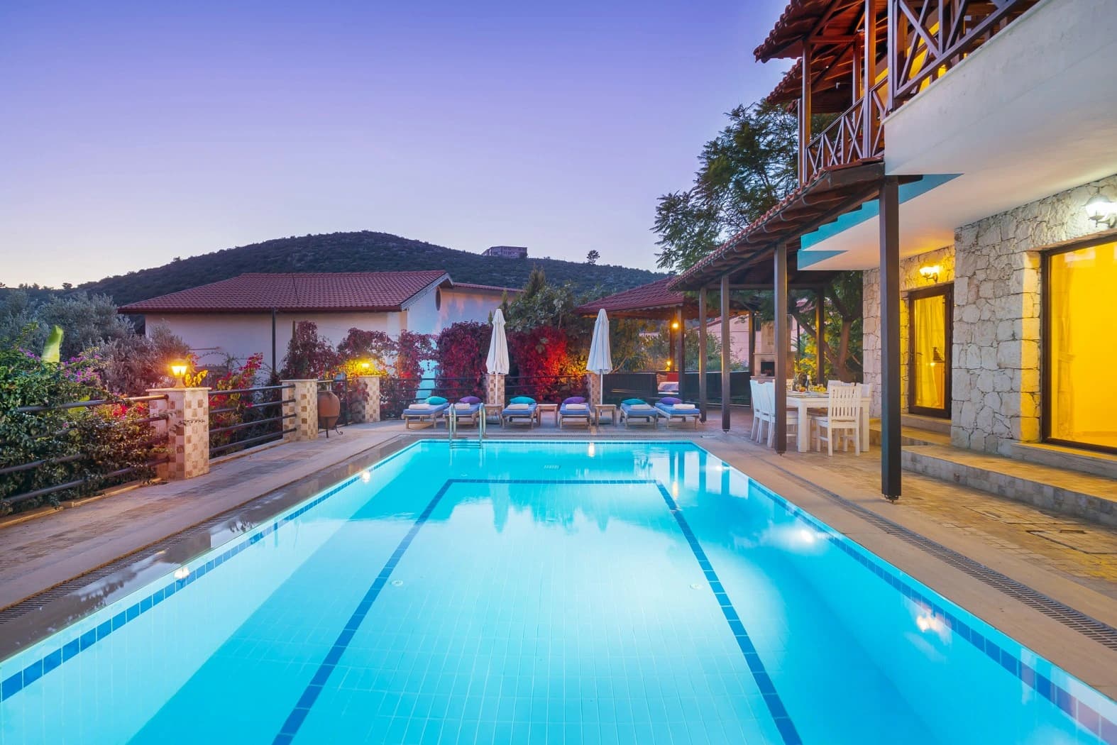 Evening shot of the lap pool with loungers, umbrellas, and mountain backdrop.