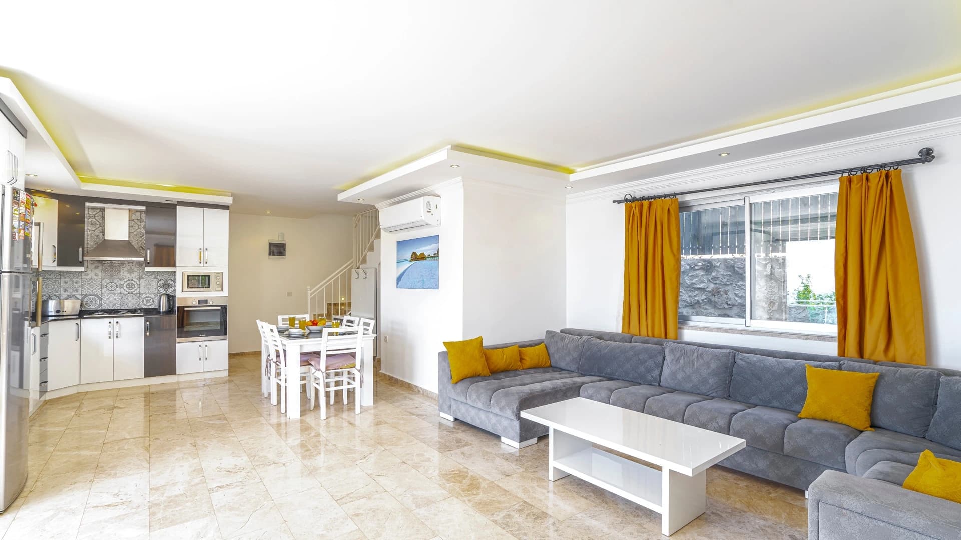 Kalkan Üzümlü'de Dağ ve Deniz Manzaralı, Isıtmalı Havuzlu, Korunaklı 2 Yatak Odalı Villa – Contemporary living room with gray sectional sofa, yellow accessories, and integrated kitchen.