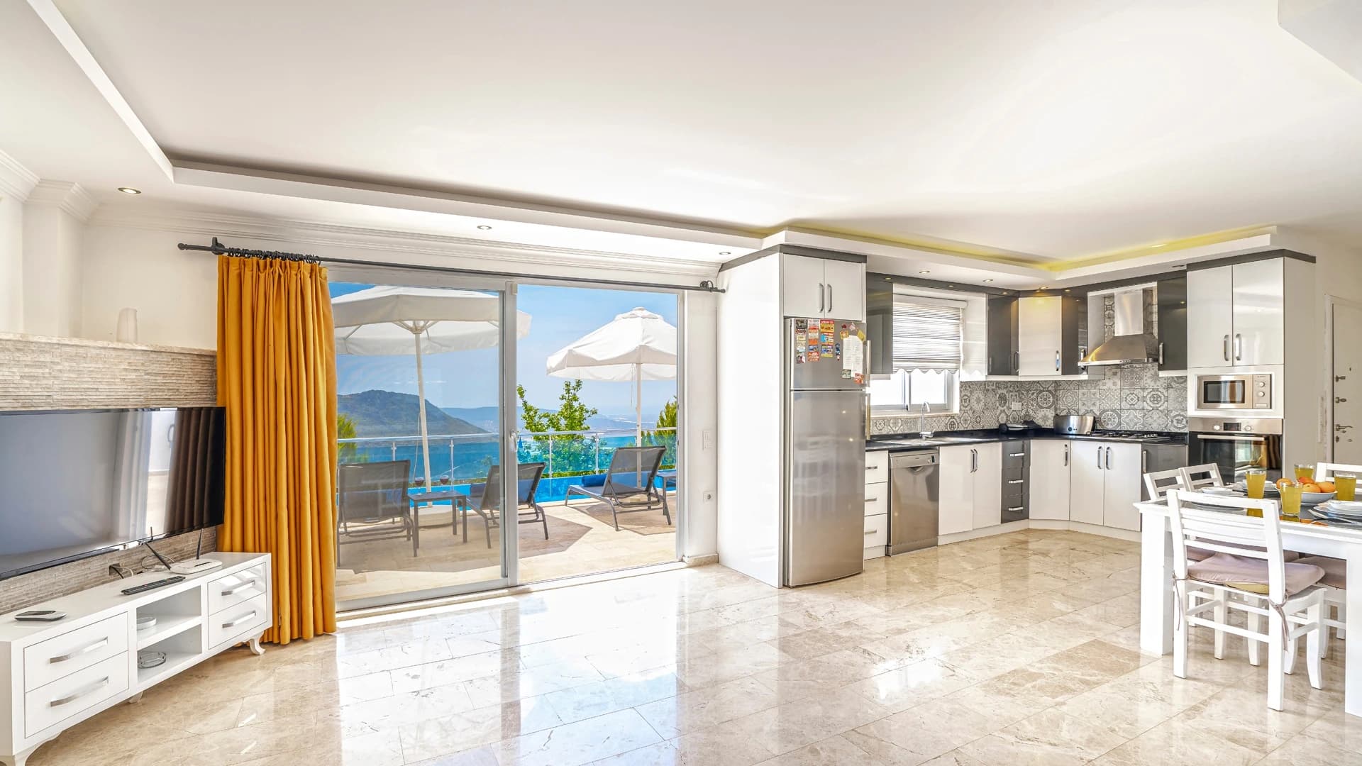Kalkan Üzümlü'de Dağ ve Deniz Manzaralı, Isıtmalı Havuzlu, Korunaklı 2 Yatak Odalı Villa – Spacious open-plan living and kitchen area with expansive sea views and access to terrace.