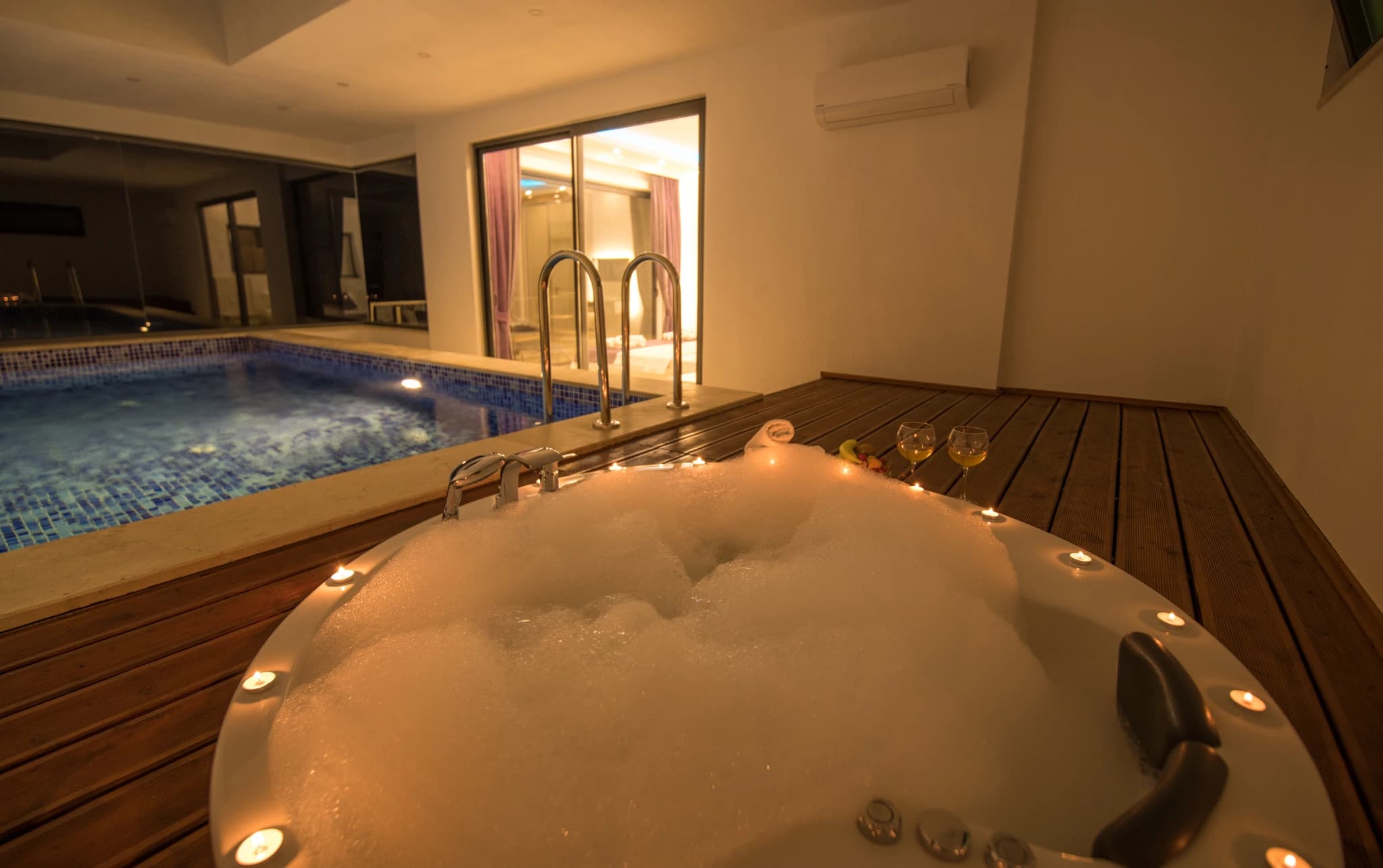Kalkan'da Özel Havuzlu ve Isıtılabilen Kapalı Havuzlu Korunaklı Balayı Villası – Luxurious indoor spa with hot tub in foreground and swimming pool, beautifully lit for evening relaxation.